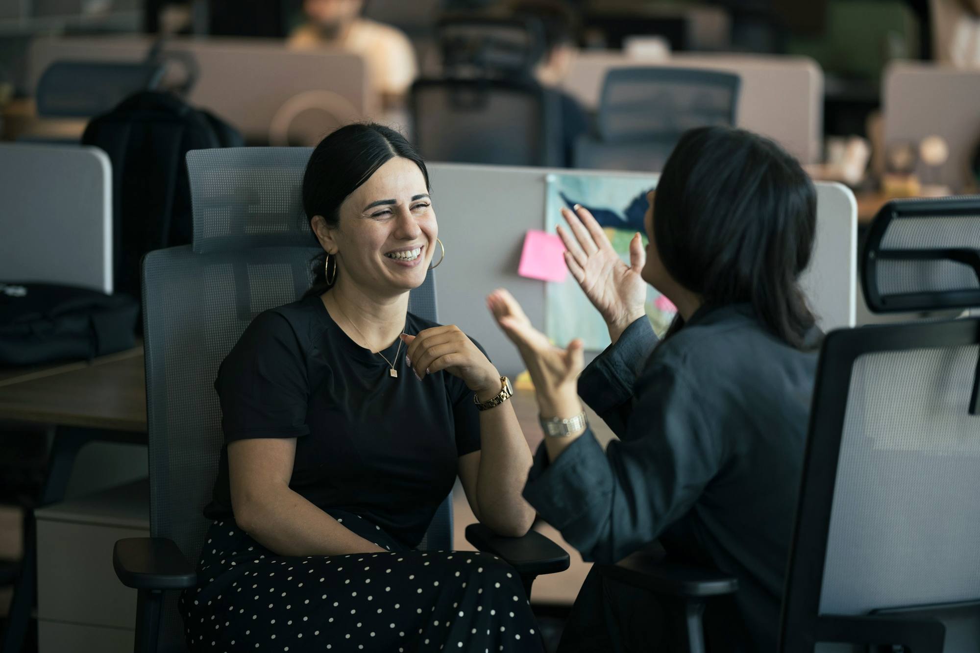 Two colleagues laughing together at a desk in an open office
