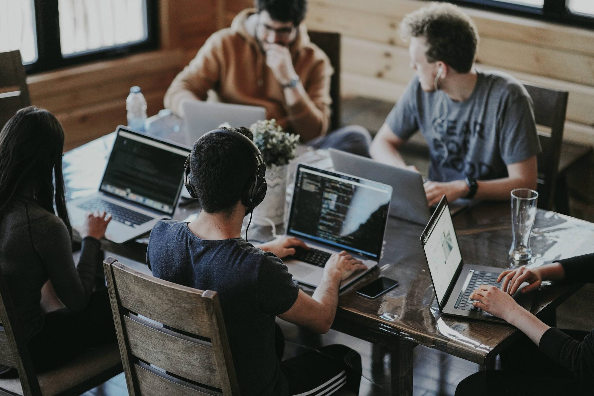 A small team working on laptops around a wooden table, seen from above