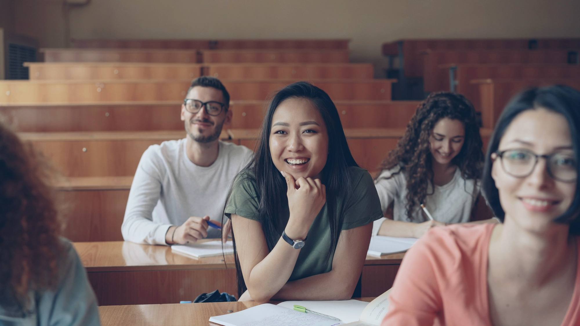Smiling students in a lecture hall, looking towards the front