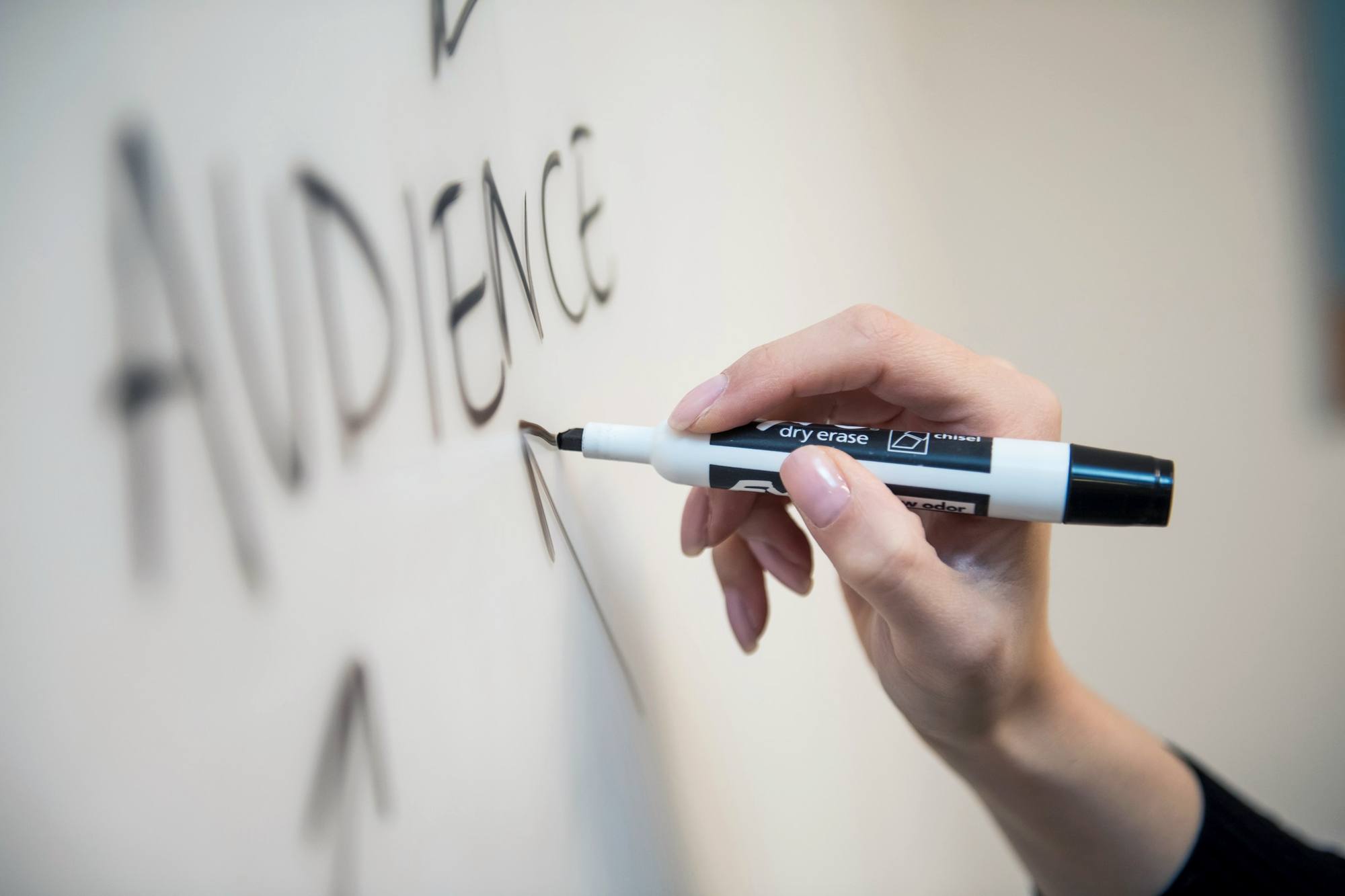 A hand writing the word “Audience” on a whiteboard