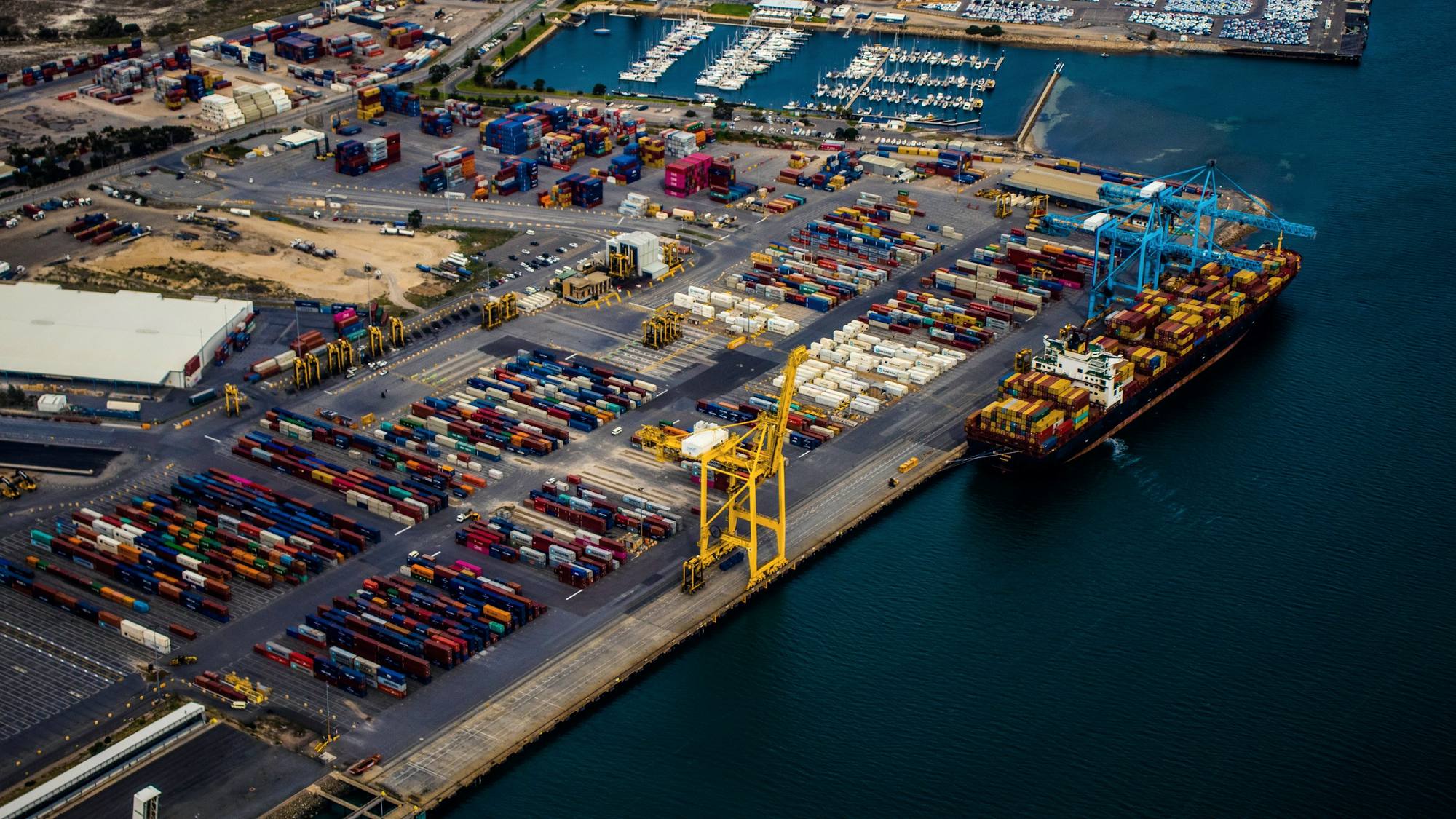 A container port seen from above, with a ship moored beside stacks of containers