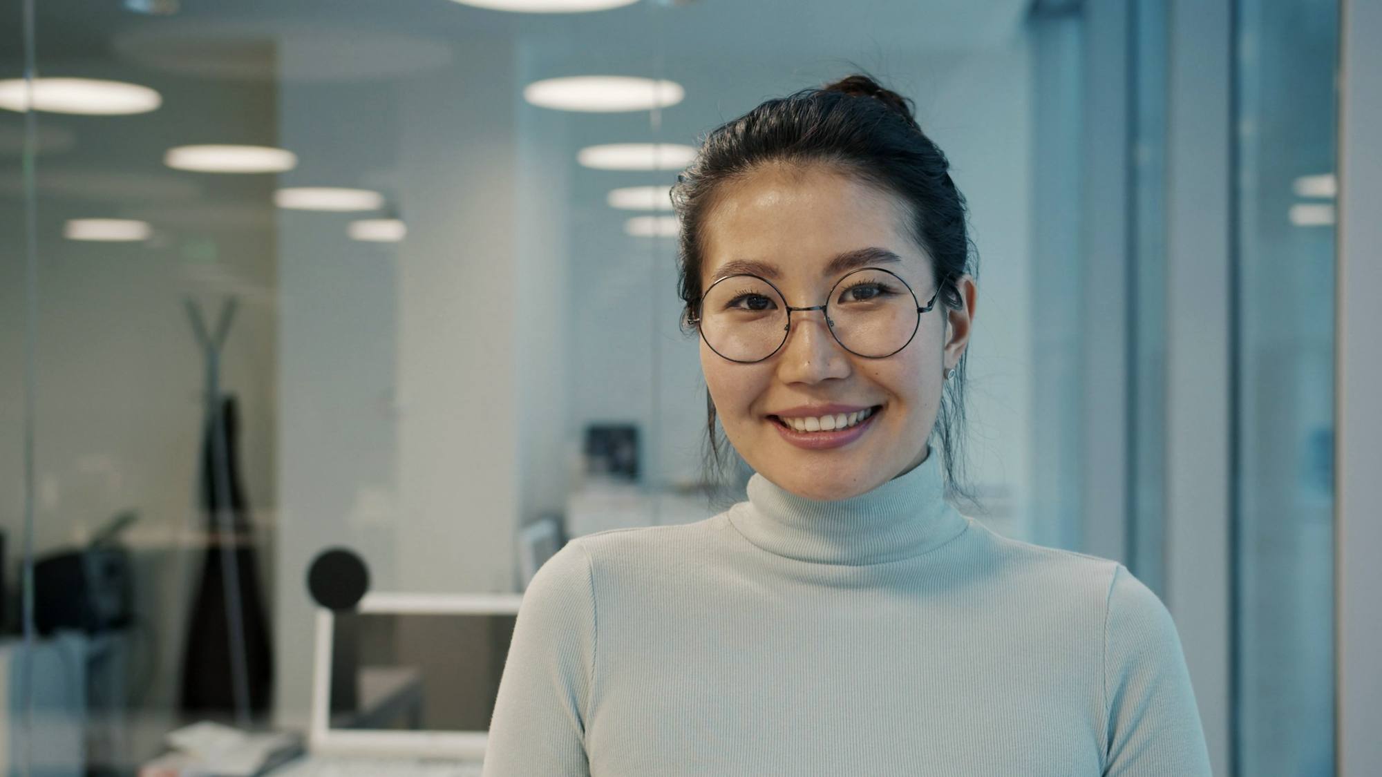 A smiling woman with round glasses in a bright office