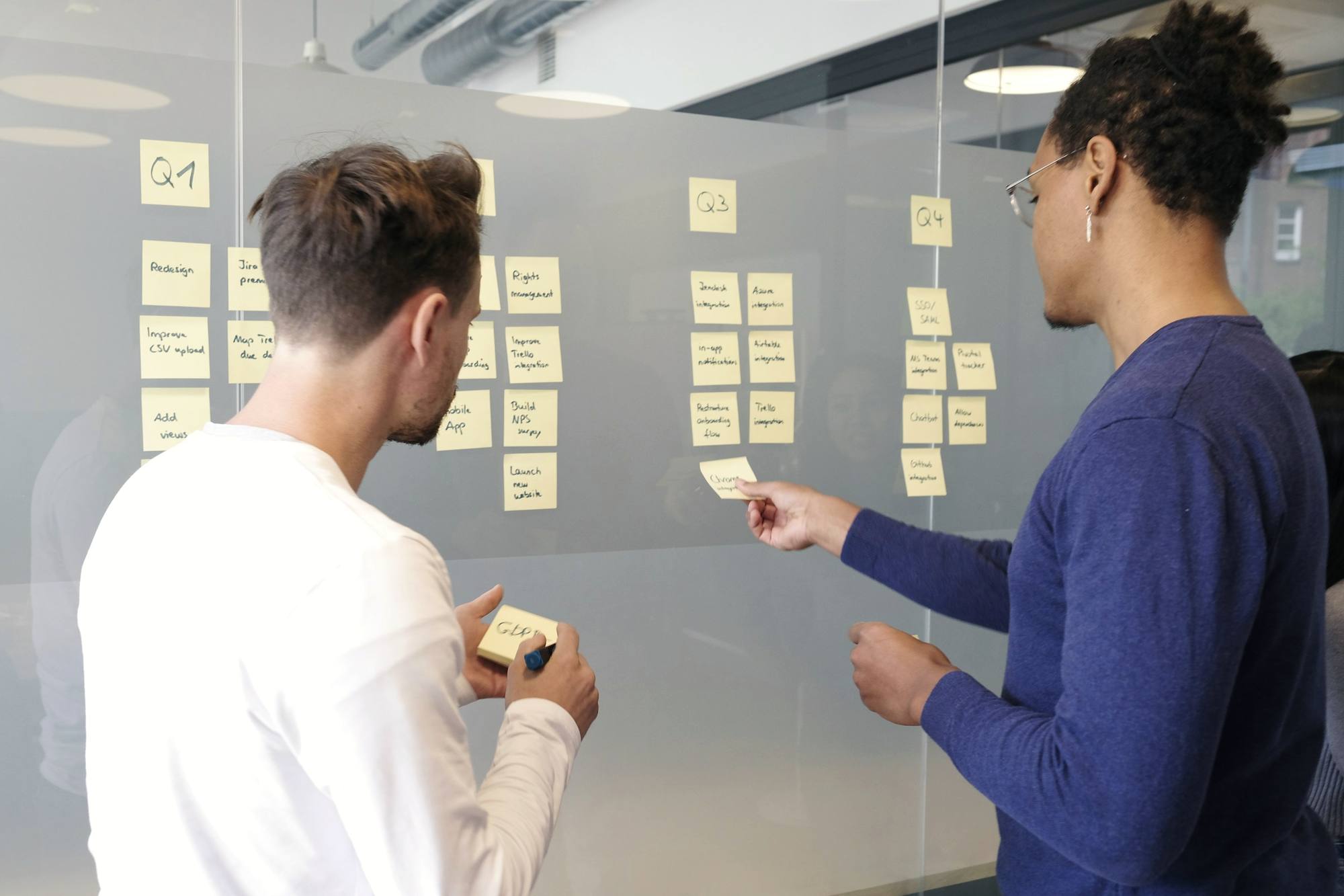Two people planning with sticky notes on a glass wall