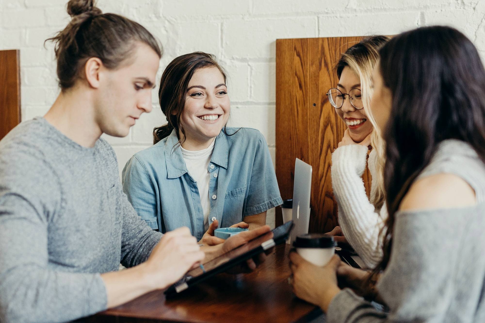Four students talking and laughing around a table with laptops