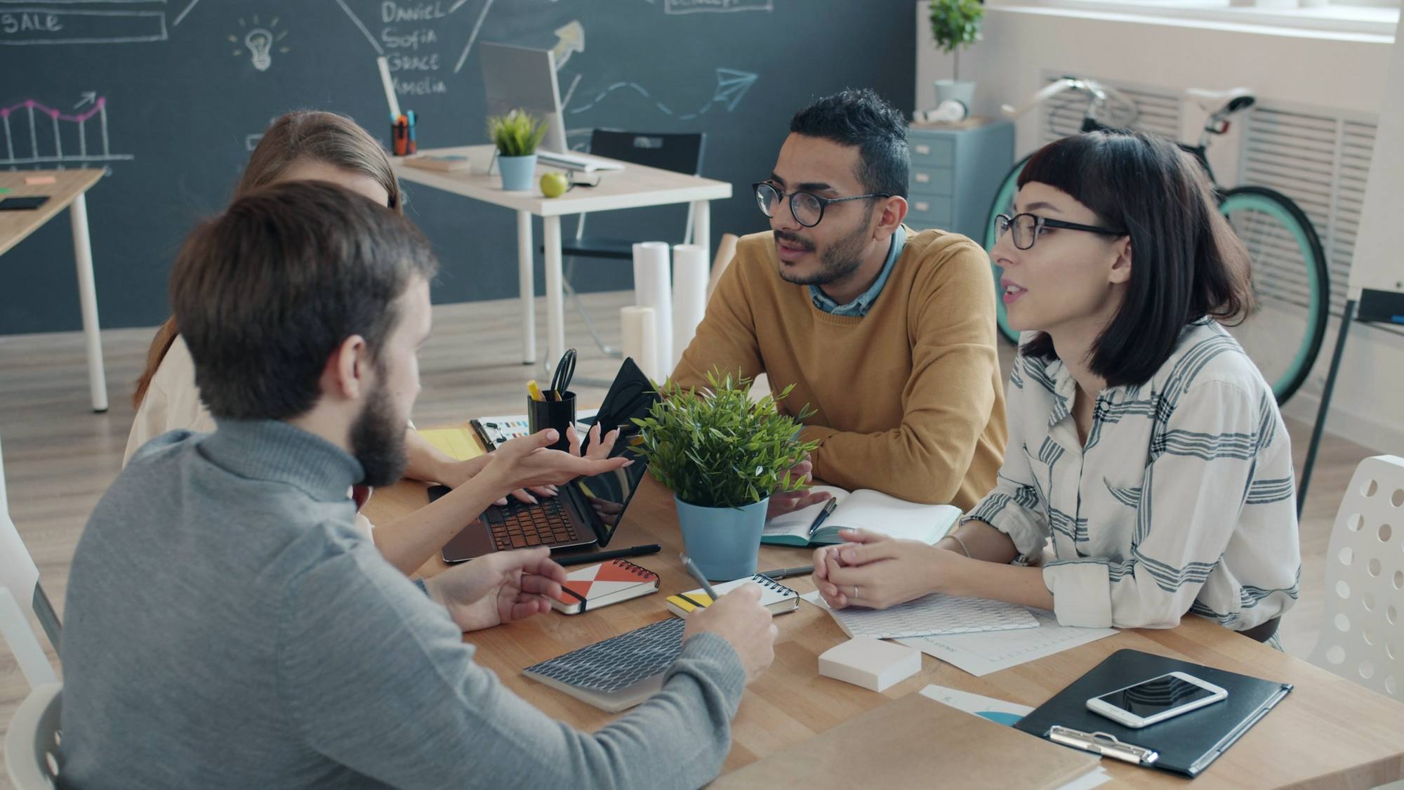 A team discussing ideas around a table with laptops and a plant