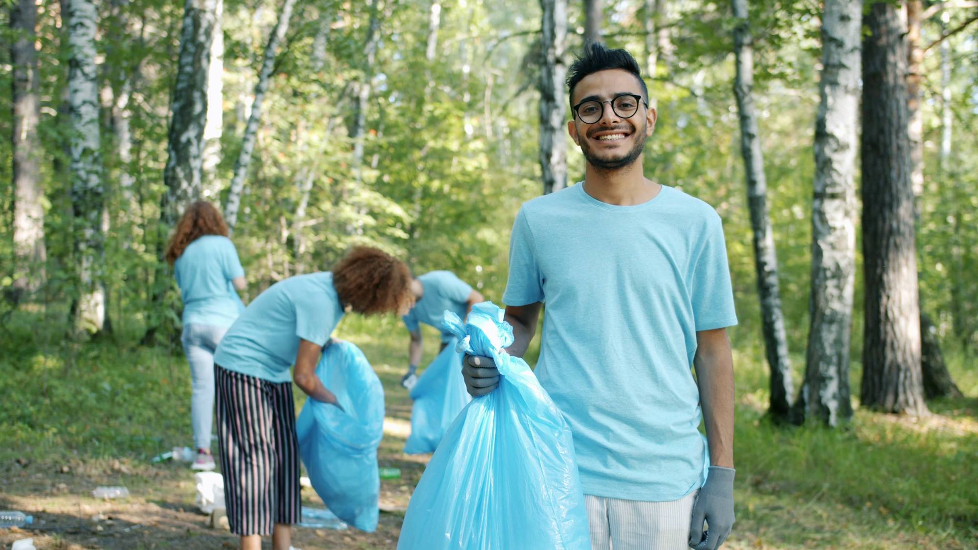 A smiling volunteer holding a rubbish bag during a clean-up in a forest